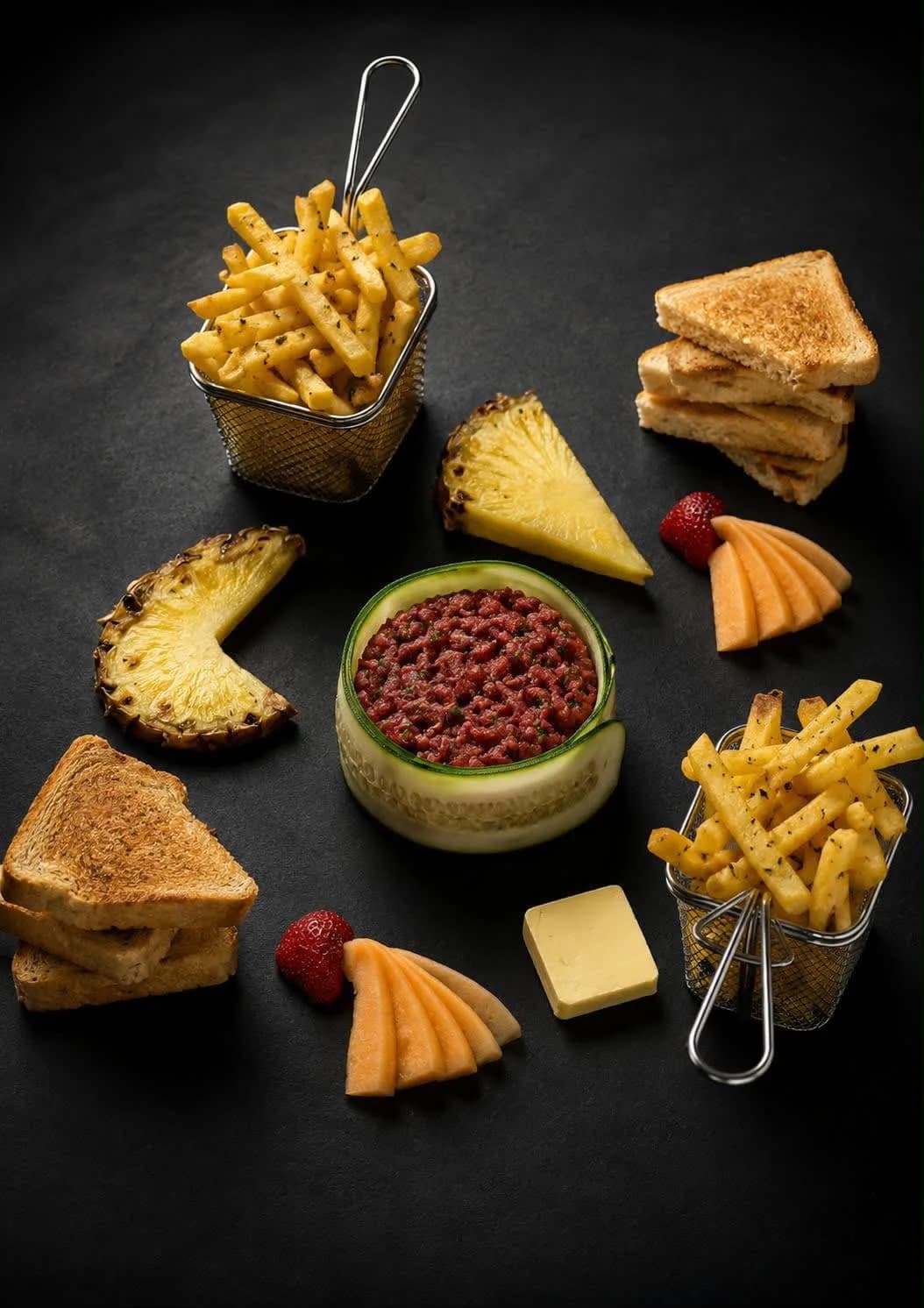 Tartare de bœuf monté en cercle de concombre, servi sur ardoise avec frites, toasts et ananas