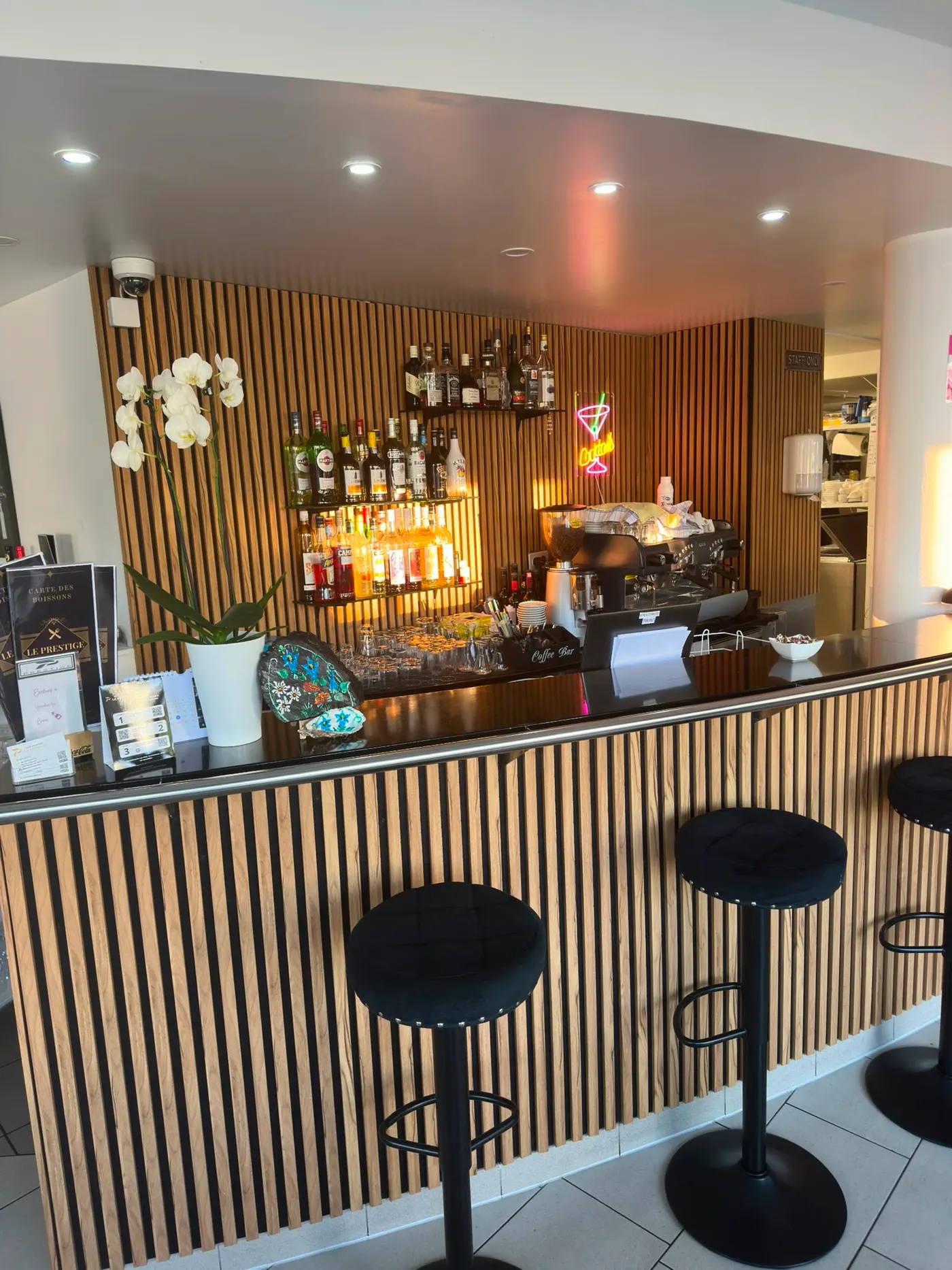 Le bar de face, les bouteilles alignées et les tabourets noirs