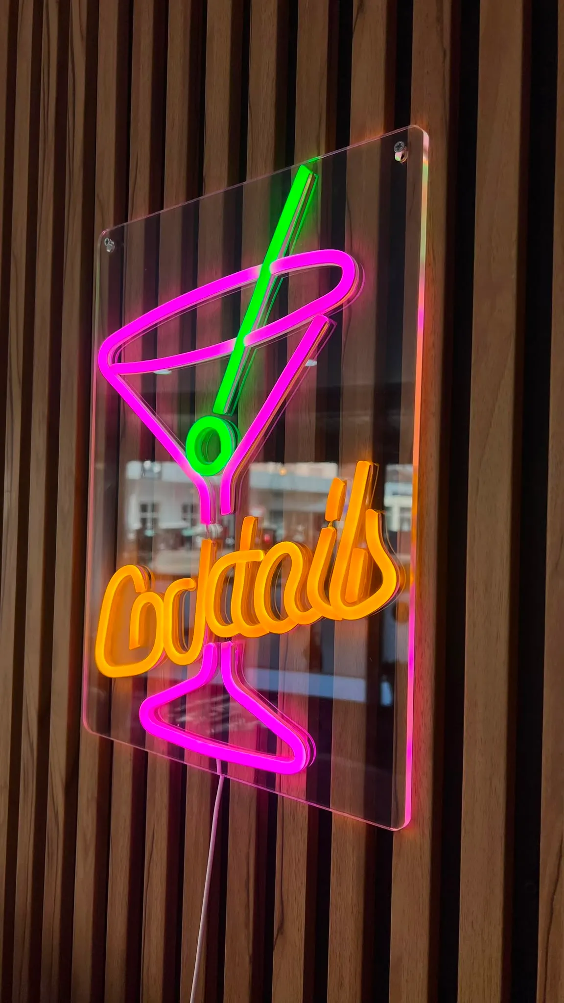 L'enseigne néon « Cocktails », rose et orange, sur le mur en tasseaux