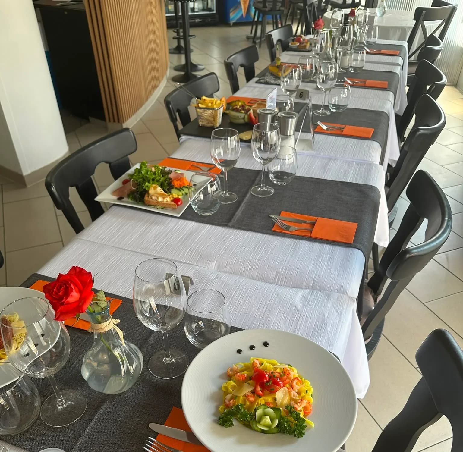 La salle dressée en enfilade, nappes blanches et serviettes orange