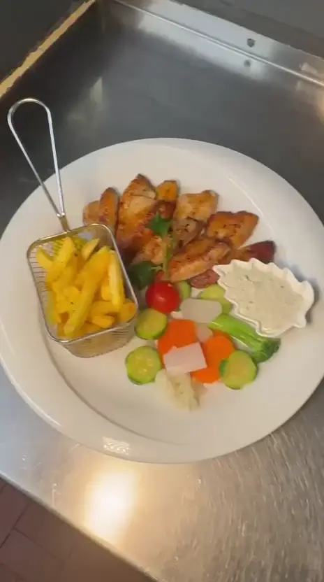 Une assiette de filets de poisson dorés en éventail, panier de frites, sauce et légumes tournés, vue en rotation lente sur le plan de travail