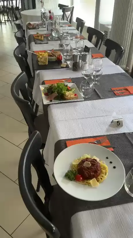 La salle dressée, longée table après table : nappes blanches, serviettes orange et assiettes servies